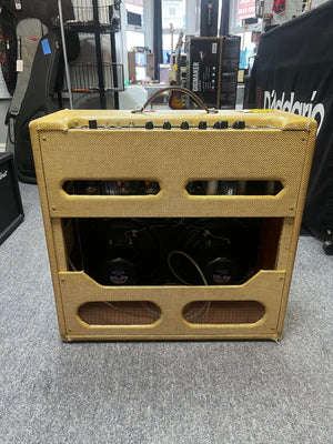 A Fender 1957 Bassman 5F6 Narrow Panel 40-Watt 4x10" Guitar Combo with tweed covering, open back, and top-mounted controls is displayed in a music store, complete with a flight case.