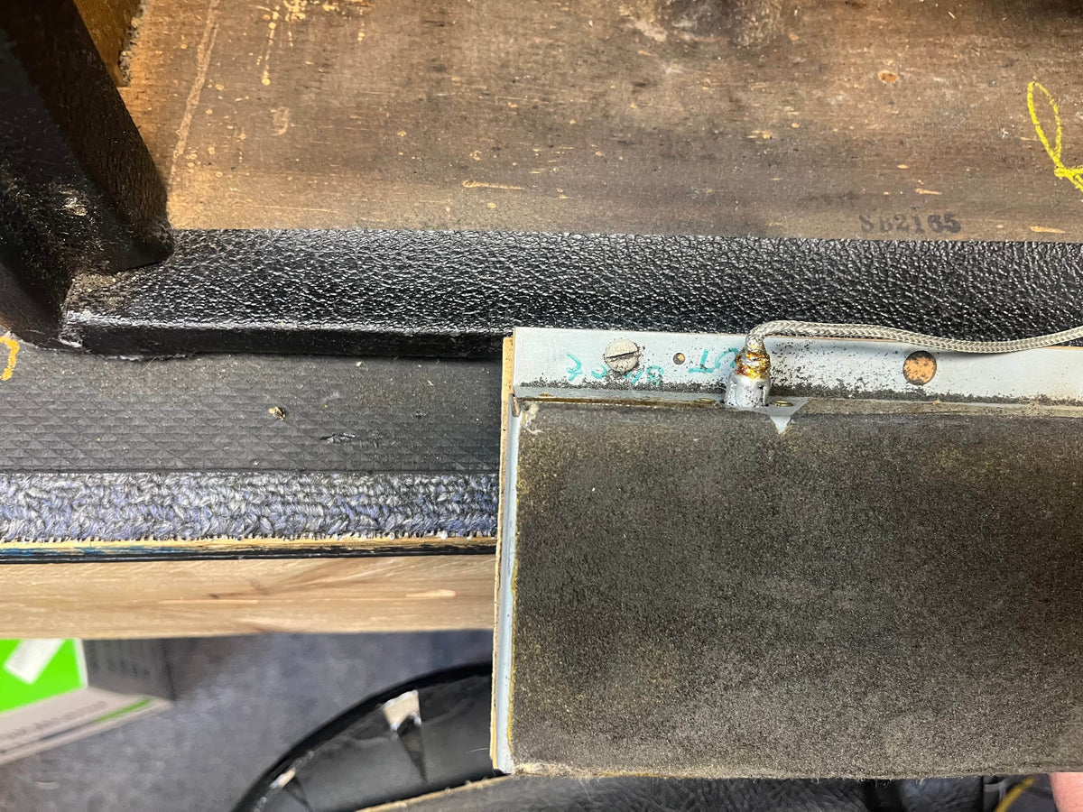 Close-up of a worn, partially detached panel with exposed wiring and screws on a textured black surface, likely part of a 1965 Fender Deluxe Reverb AB763 Pre-CBS Blackface (serial A 06439) amplifier by Fender.