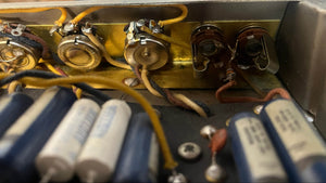 Close-up of electronic components like potentiometers, capacitors, and wiring inside the metal casing of a vintage Fender 1965 Deluxe Reverb AB763 Pre-CBS Blackface Serial A 06439 amplifier.