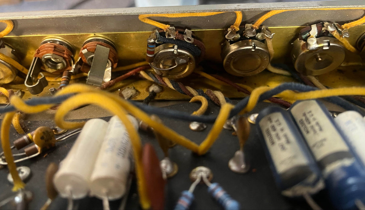Close-up of electronic components inside a 1965 Fender Deluxe Reverb AB763 (Pre-CBS Blackface, Serial A 06439), showing capacitors, resistors, potentiometers, and yellow wiring—a classic vintage Fender amp.