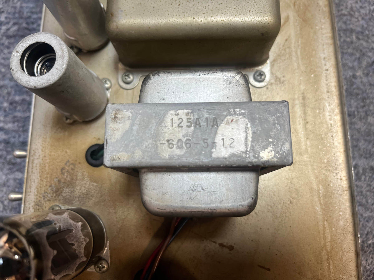 Close-up of a metal transformer labeled "125A1A 606-5-12" mounted on a dusty vintage 1965 Fender Deluxe Reverb AB763 Pre-CBS Blackface (serial A 06439) tube amp with visible tubes and wires.