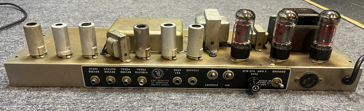 Rear view of a Fender 1965 Deluxe Reverb AB763 Pre-CBS Blackface (Serial A 06439) shows vacuum tubes, transformers, and input/output jacks on a grey carpet—classic vintage amp details.