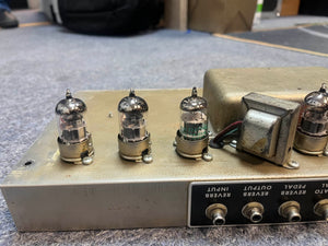 Close-up of a 1965 Fender Deluxe Reverb AB763 (Pre-CBS Blackface, Serial A 06439) tube amp with four vacuum tubes and metal casing, showing wiring and labeled input/output jacks on a carpeted floor.