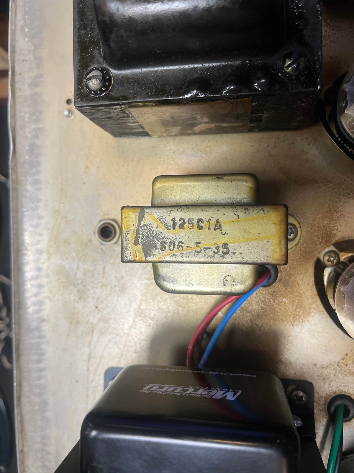 Close-up of a metal electronic component labeled "125C1A 606-5-35" with colored wires, mounted on a dusty surface—part of the 1965 Fender Super Reverb - Black Panel, available for local pickup at Guitars on Main.
