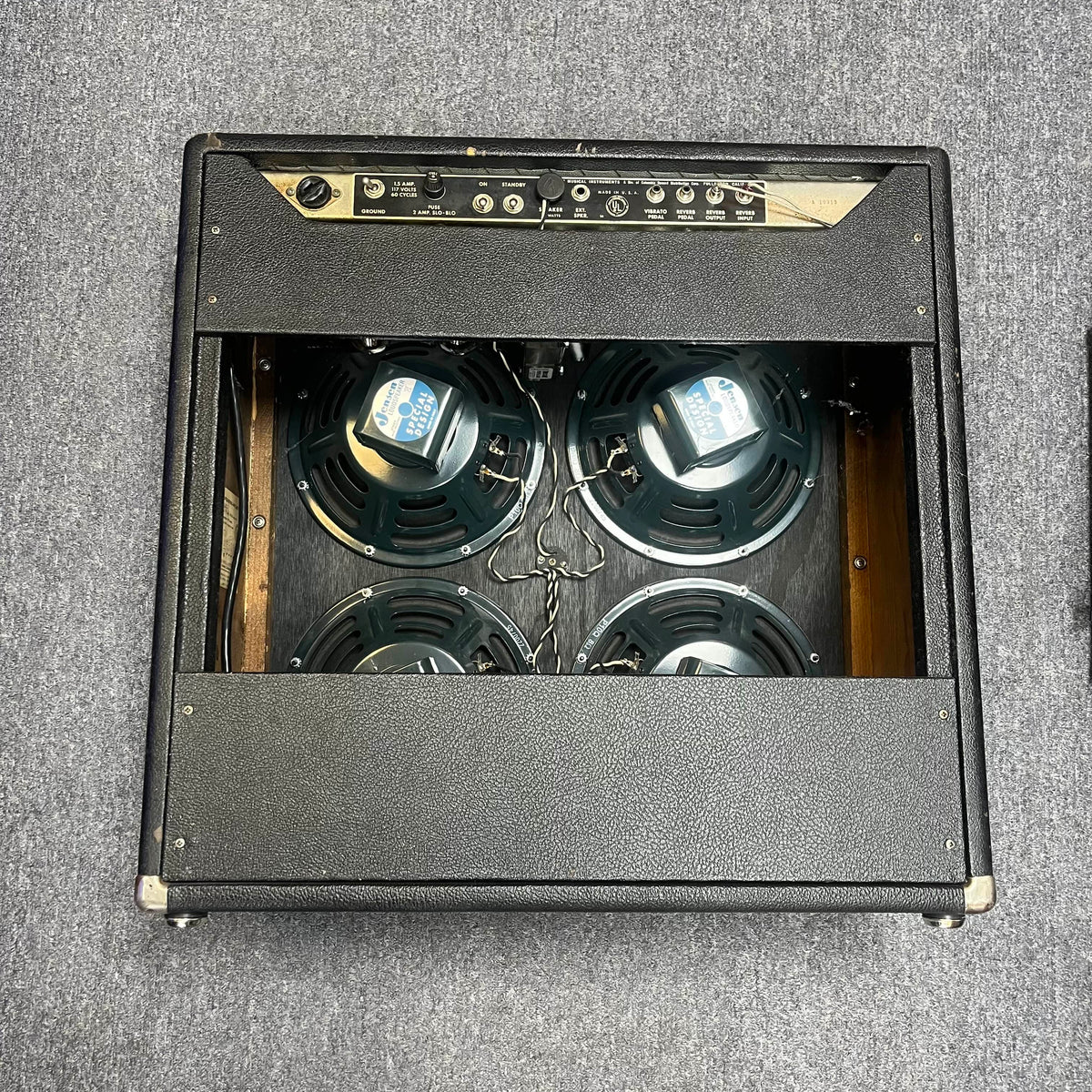 The 1965 Fender Super Reverb - Black Panel, offered by Guitars on Main, showcases four speakers behind a rear open panel and classic wiring, all set on a gray carpet. Local pickup available; enjoy iconic vintage sound and style.
