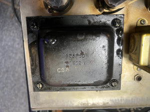 Close-up of a metal component from a 1965 Fender Super Reverb - Black Panel, available for local pickup at Guitars on Main, with "125P50," "606521," and "CSA 11751" stamped on its surface and attached by four screws.