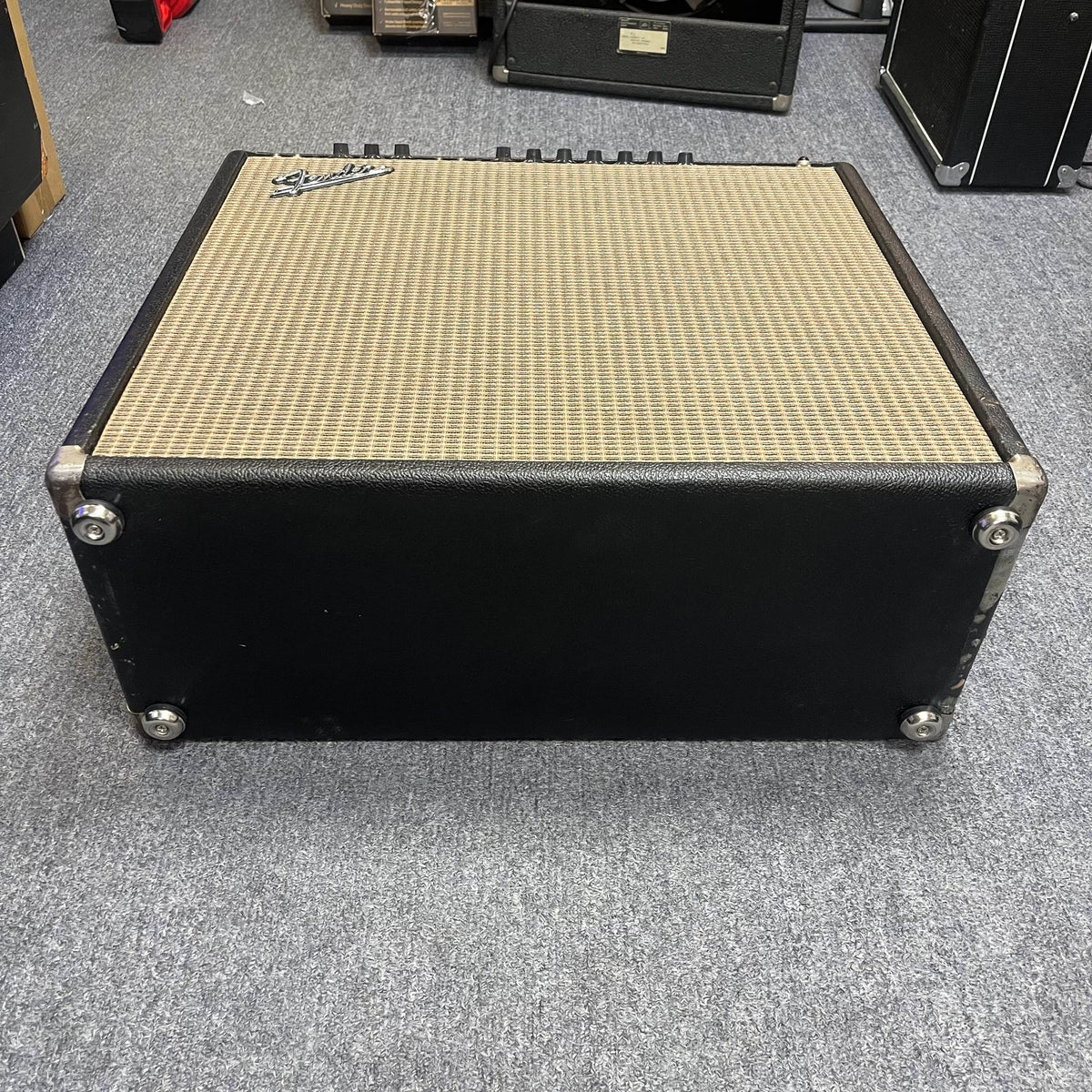 A 1965 Fender Super Reverb - Black Panel from Guitars on Main, this vintage black guitar amp with a beige grille is shown on a gray carpeted floor, viewed from the front and slightly above. Local pickup available.