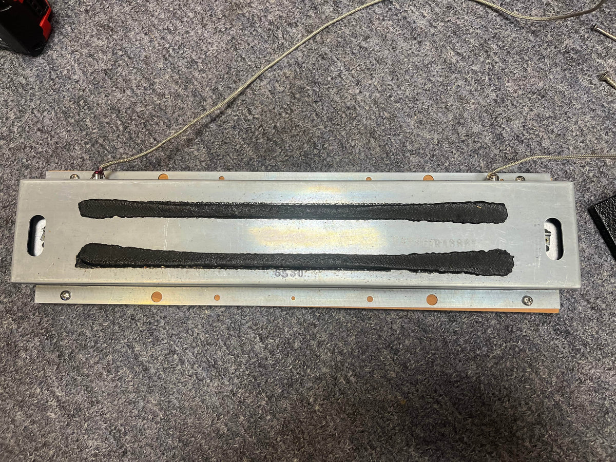 A reverb tank of a 1965 Fender Super Reverb - Black Panel - "Player’s Dream" Restoration by Guitars on Main, placed on gray carpet with attached wires.