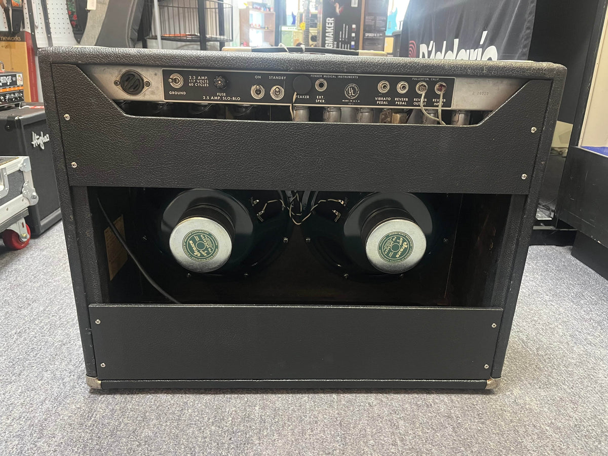 The back of a 1966 Fender Twin Reverb 2-Channel 85-Watt 2x12" Guitar Combo Amp w/Flight Case shows twin speakers, control panel with jacks and knobs, tubes, and spring reverb displayed inside a music equipment store.
