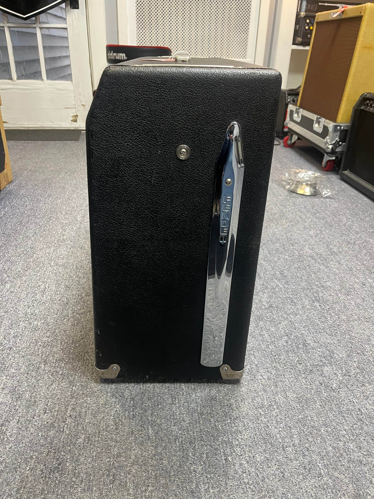 A 1966 Fender Twin Reverb 2-Channel 85-Watt 2x12" Guitar Combo Amp by Fender, with a chrome handle and flight case, sits on a gray carpeted floor among other musical gear.