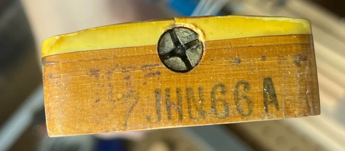 Close-up of a wooden part with a yellow top and metal screw, showing faded "JINNGG A" text—likely an original pickup from a Fender 1966 Jazz Bass Natural Refinish w/Case.