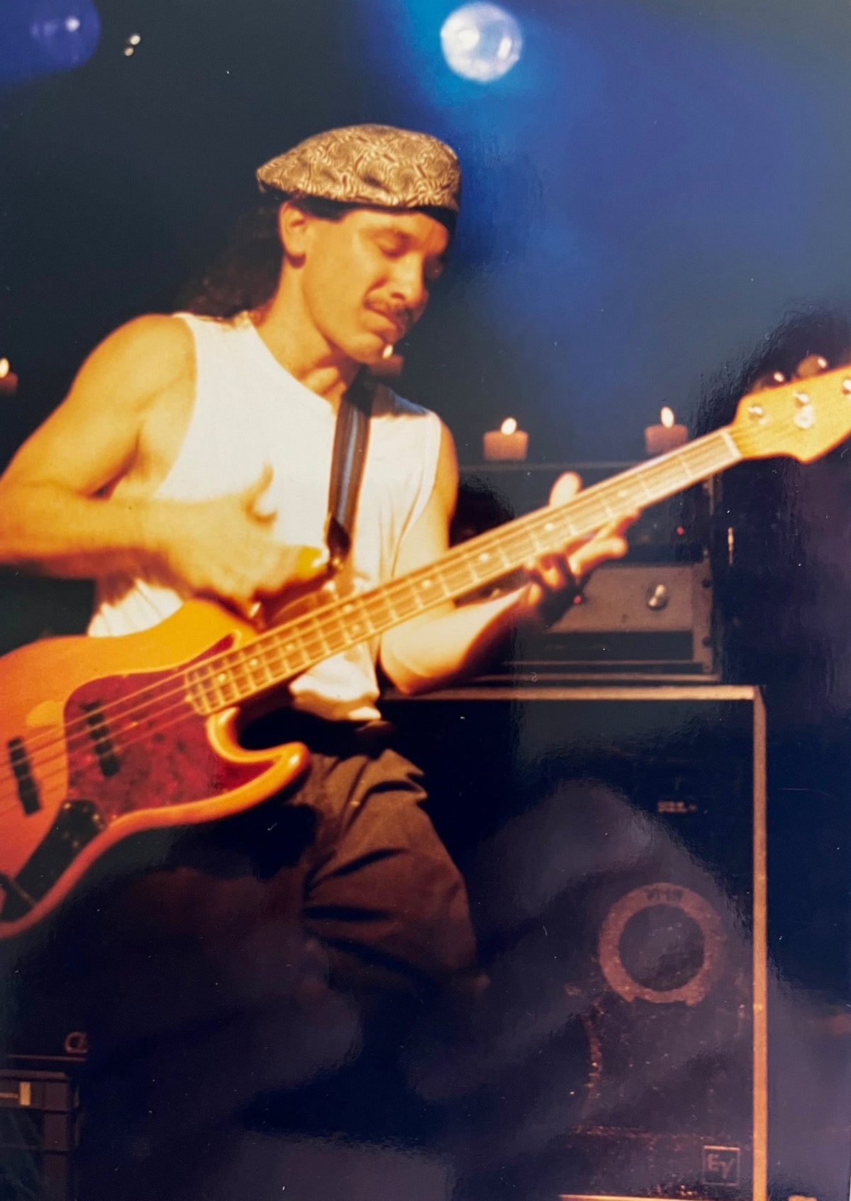 A musician in a sleeveless shirt and bandana plays a Fender 1966 Jazz Bass Natural Refinish w/Case on stage, surrounded by amplifiers and stage lights.