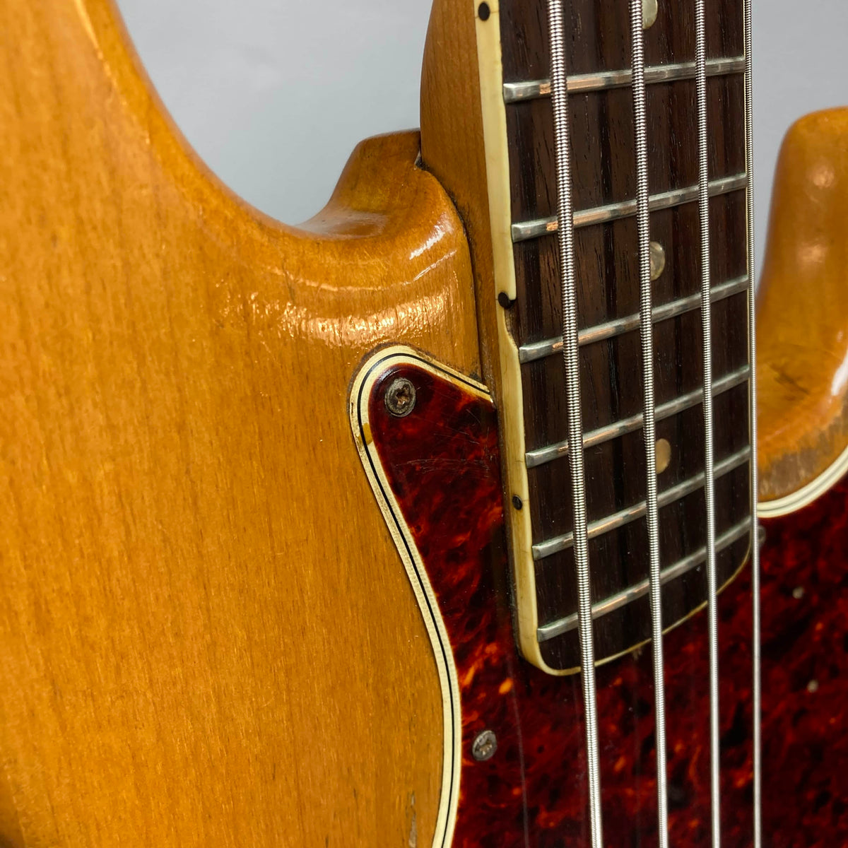 Close-up of a 1966 Fender Jazz Bass Natural Refinish by Fender, showing the body with pickguard edge, strings, and fingerboard frets. Includes case.