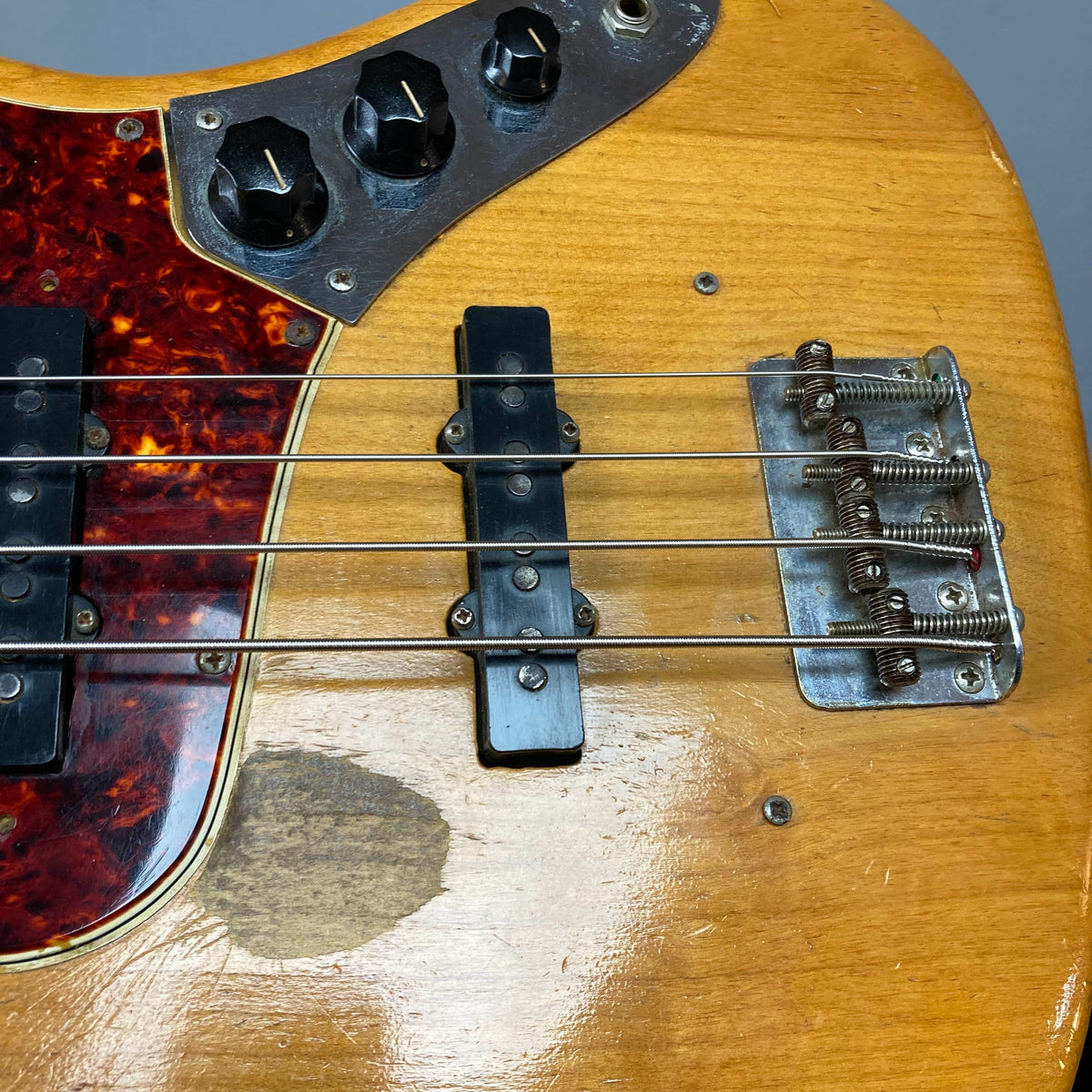 Close-up of a Fender 1966 Jazz Bass Natural Refinish, showing four strings, original pickups, control knobs, bridge, and a worn area on the wood finish. Includes case.