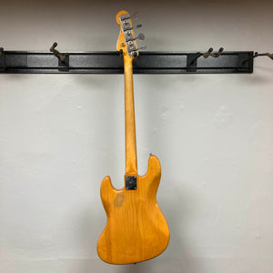 A 1966 Fender Jazz Bass Natural Refinish by Fender hangs by its headstock on a black wall rack, displayed from the back to highlight its natural finish. Includes case.