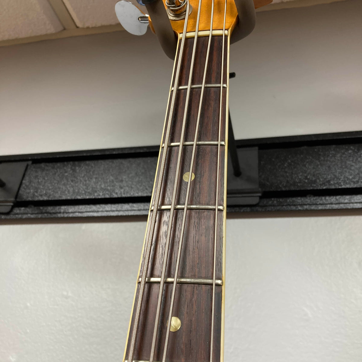 Close-up of a 1966 Fender Jazz Bass Natural Refinish neck and fretboard, showing metal frets, dot inlays, and part of the headstock against a white wall. Includes case.
