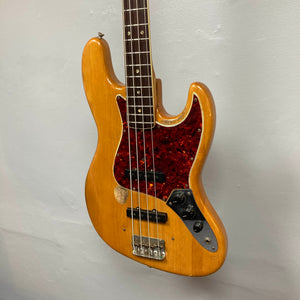 A 1966 Fender Jazz Bass Natural Refinish by Fender with original pickups, a red tortoiseshell pickguard, visible string wear, and mounted on a light wall; includes case.
