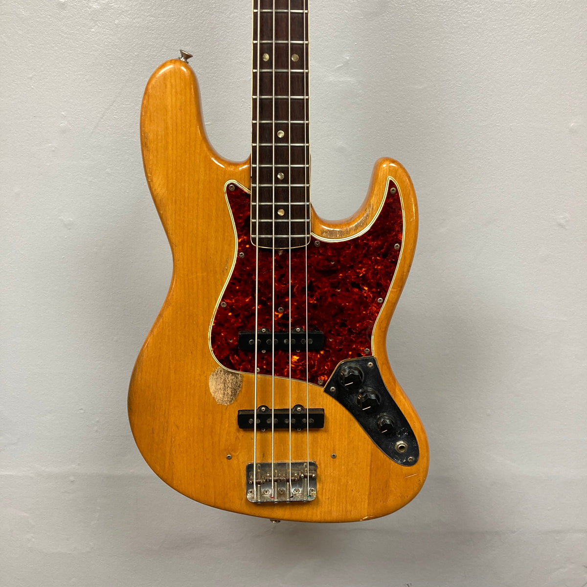 The 1966 Fender Jazz Bass Natural Refinish w/Case by Fender features a red tortoiseshell pickguard, original pickups, and visible bridge wear, shown against a plain light gray background.