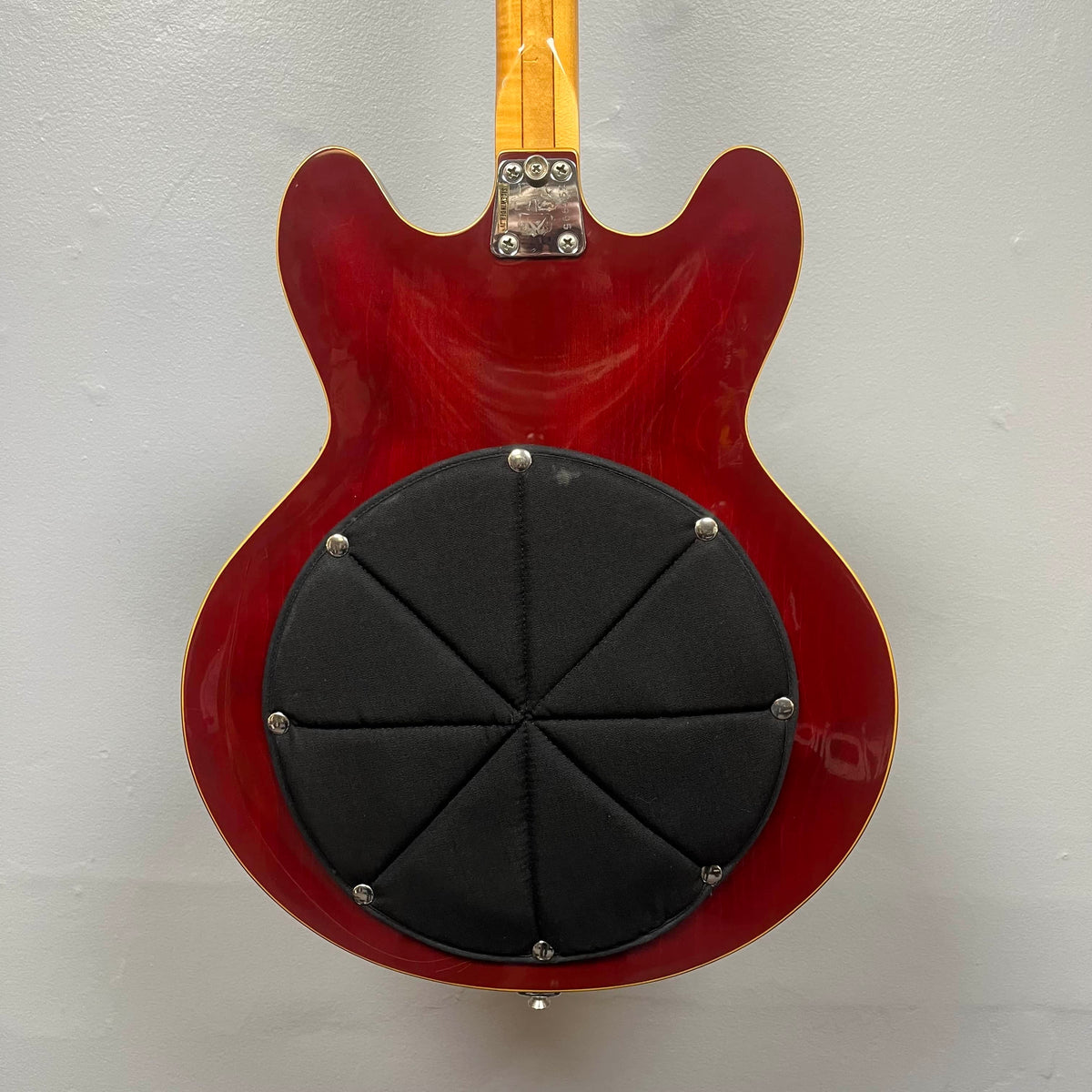 The back of a cherry 1967-68 Vox Sidewinder IV Bass (V272) by Vox features a large, black, padded circular attachment covering the semi-hollow body.