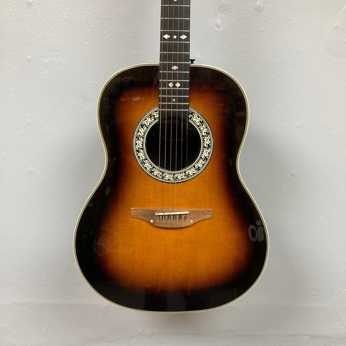 USA-made 1976 Ovation 1112-1 Acoustic Guitar w/Case, featuring a sunburst finish, ornate soundhole rosette, white fretboard inlays, and Lyrachord rounded back, photographed against a plain light-colored wall.