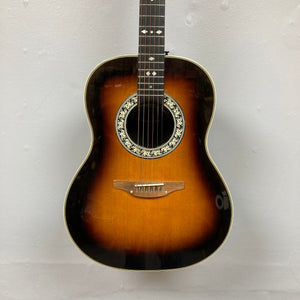 USA-made 1976 Ovation 1112-1 Acoustic Guitar w/Case, featuring a sunburst finish, ornate soundhole rosette, white fretboard inlays, and Lyrachord rounded back, photographed against a plain light-colored wall.