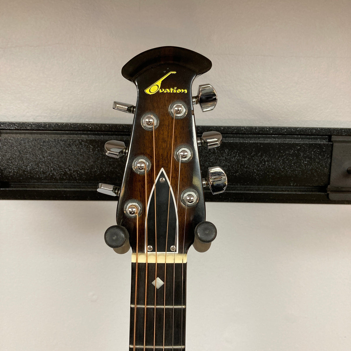 Close-up of the headstock on a 1976 Ovation 1112-1 Acoustic Guitar w/Case USA Consign, showing tuning pegs, Ovation logo, and part of the fretboard with a plain wall background.
