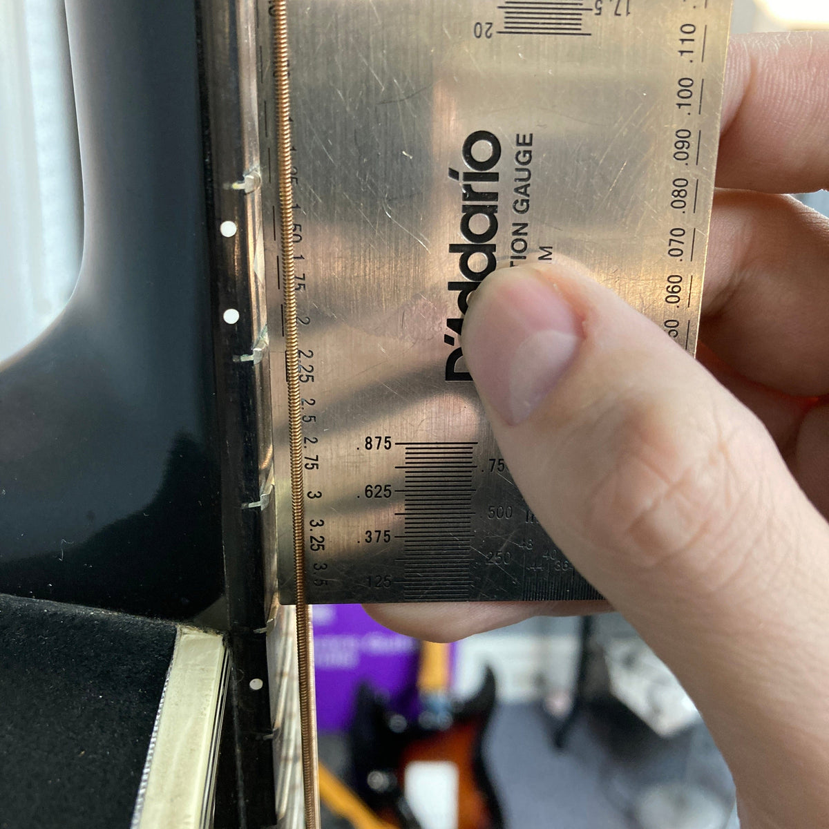 A hand uses a D'Addario string action gauge to measure string height on a 1976 Ovation 1112-1 Acoustic Guitar w/Case USA Consign, a classic Ovation model with a Lyrachord rounded back.