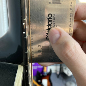 A hand uses a D'Addario string action gauge to measure string height on a 1976 Ovation 1112-1 Acoustic Guitar w/Case USA Consign, a classic Ovation model with a Lyrachord rounded back.