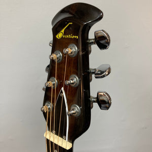 Close-up of the headstock of a 1976 Ovation 1112-1 Acoustic Guitar w/Case USA Consign, featuring six tuning pegs, strings, and the Ovation logo on a dark wood finish.