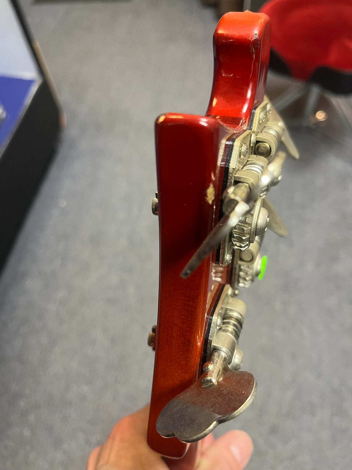 Close-up of a person holding the headstock of a 1978 Rickenbacker 4001 Bass — Fireglo (Serial RL7346), showing tuning pegs, minor scratches on the red wood, and highlighting its classic finish.