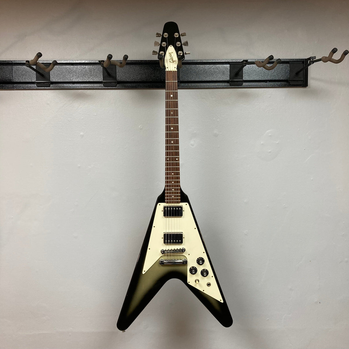 1979 Gibson Flying V Silverburst guitar on wall hook with original case, showcasing a unique vintage design and minor blemishes.