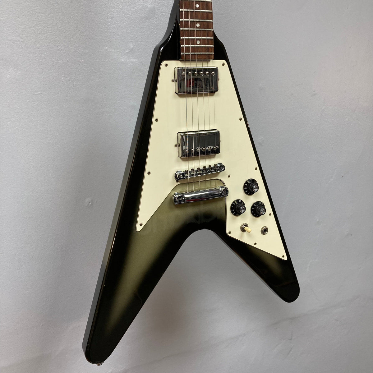 1979 Gibson Flying V Silverburst guitar displayed on a wall, featuring minor blemishes and original case.