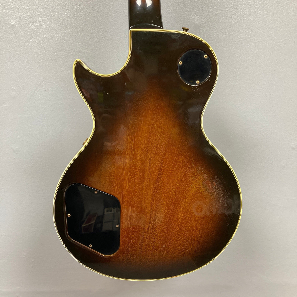 The back of the 1980 Gibson Les Paul Custom – Tobacco Sunburst w/OHSC features a single cutaway, cream binding, and two black rear cavity covers, showcased against a plain white wall—evoking classic Gibson style.