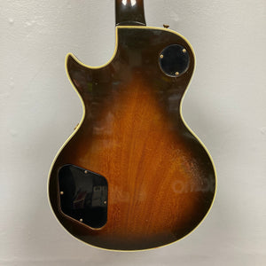 The back of the 1980 Gibson Les Paul Custom – Tobacco Sunburst w/OHSC features a single cutaway, cream binding, and two black rear cavity covers, showcased against a plain white wall—evoking classic Gibson style.
