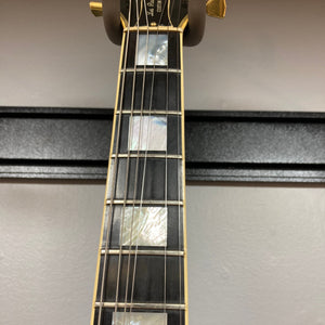 Close-up of a Gibson 1980 Les Paul Custom – Tobacco Sunburst w/OHSC neck, highlighting mother-of-pearl inlays, six strings, and gold tuners against a light gray wall—a striking vintage guitar from Gibson.