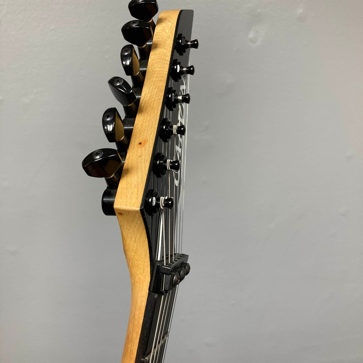 Close-up of a 1992 Carvin Ultra V USA headstock with six tuners and metal strings, featuring a Kahler Steeler Trem and MJ-wound Seymour Duncan DCJ, set against a plain light-colored wall.