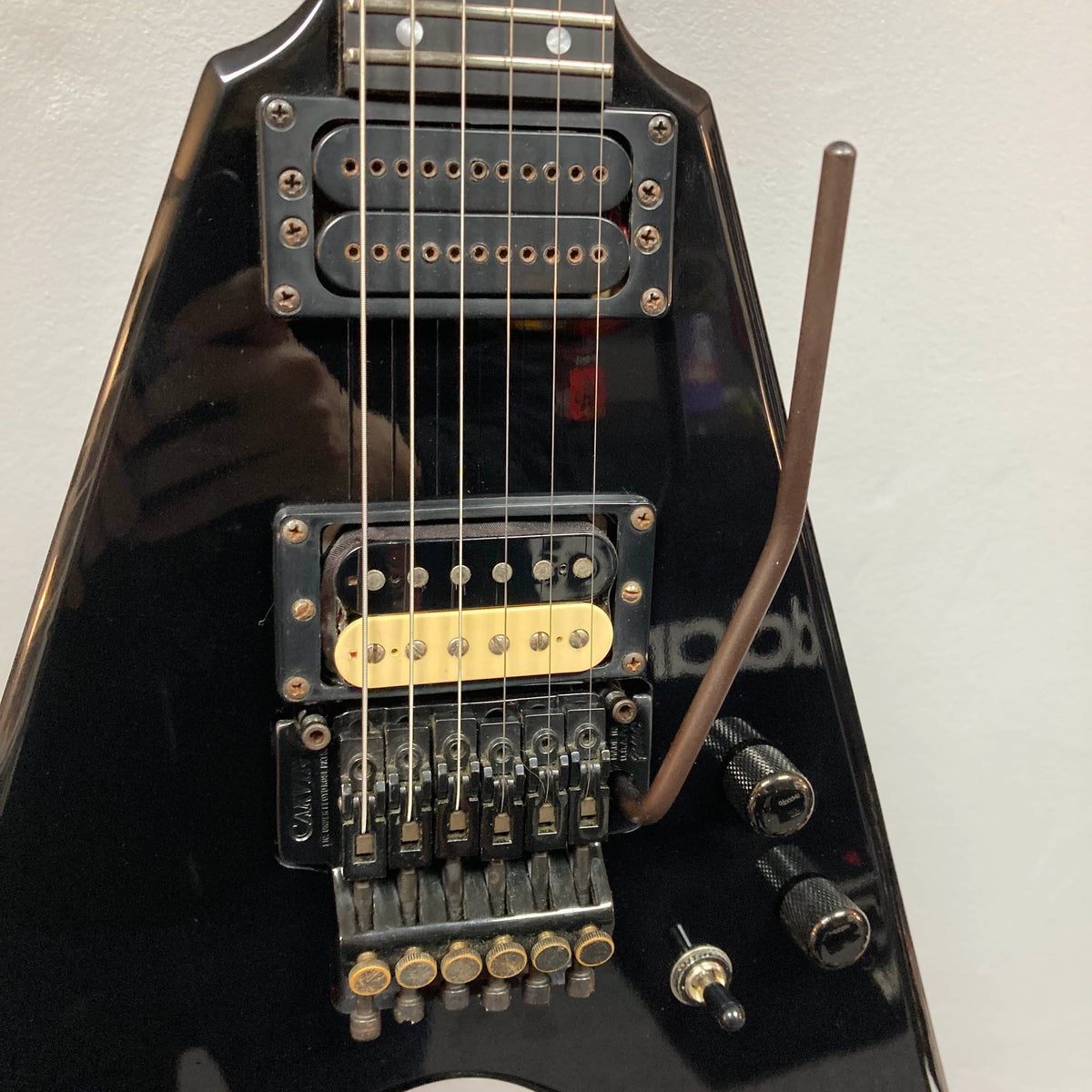 Close-up of a 1992 Carvin Ultra V USA electric guitar featuring a Kahler Steeler tremolo and MJ-wound Seymour Duncan DCJ humbucker on its sleek black body, with bridge, control knobs, output jack, and tremolo arm in view.