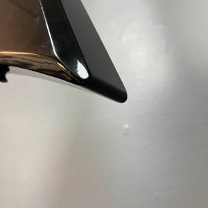 Close-up of the shiny black tip of a metallic object, likely from a Carvin 1992 Ultra V USA with Kahler Steeler Trem and MJ-wound Seymour Duncan DCJ, set against a plain light gray background.