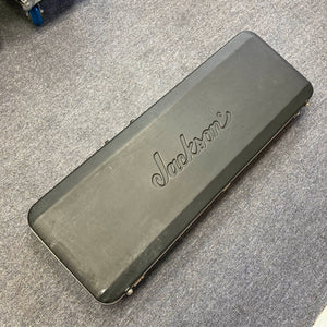 A black Jackson hard guitar case, featuring the “Jackson” logo and made for the 1995 Jackson SL1 Soloist Custom Shop Eerie Dess Swirl w/Case, is lying closed on a gray carpeted floor.