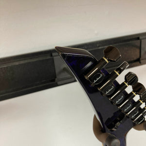 Close-up of the headstock of a Jackson 1995 SL1 Soloist Custom Shop Eerie Dess Swirl electric guitar, featuring black tuning pegs, mounted on a wall hanger against a white wall.