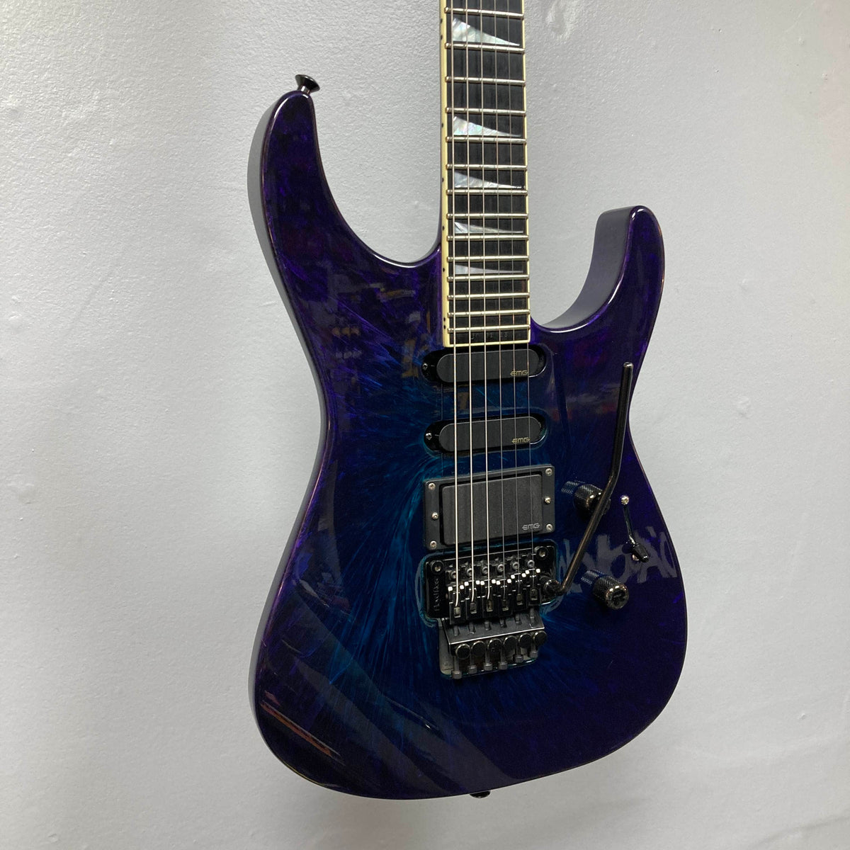 Featuring a mesmerizing Eerie Dess Swirl finish in dark blue with a glossy sheen, the 1995 Jackson SL1 Soloist Custom Shop electric guitar boasts two humbucker pickups, a locking tremolo bridge, and sleek black hardware. This exceptional Jackson instrument comes complete with its case and is captured here against a plain white wall.