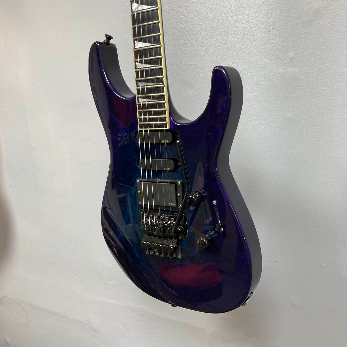A Jackson 1995 SL1 Soloist Custom Shop electric guitar in Eerie Dess Swirl, featuring a glossy purple finish, three pickups, a tremolo bridge, and black knobs is hanging against a white wall.