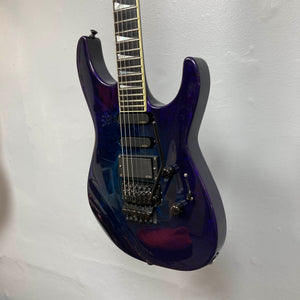 A Jackson 1995 SL1 Soloist Custom Shop electric guitar in Eerie Dess Swirl, featuring a glossy purple finish, three pickups, a tremolo bridge, and black knobs is hanging against a white wall.