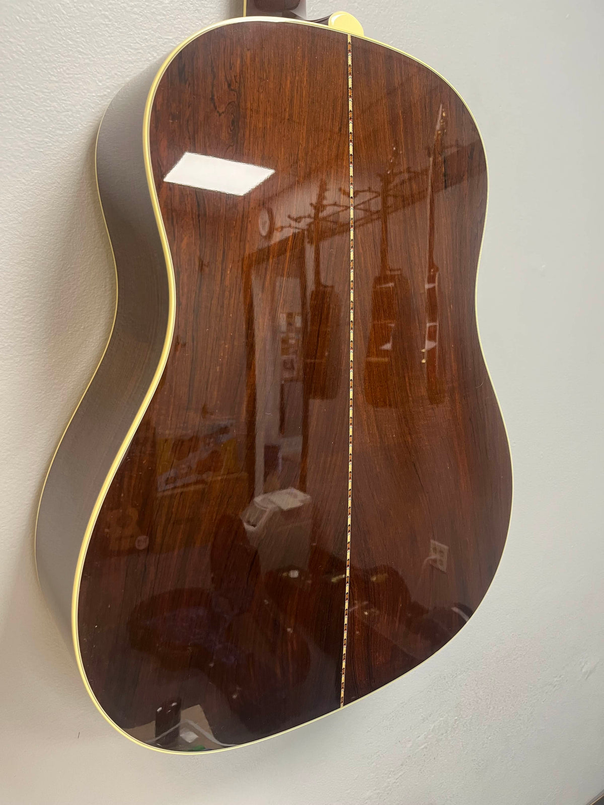 A close-up of the back of a 2005 Collings CJ BaA—Brazilian Rosewood & Adirondack Spruce—shows its glossy finish, light binding, and reflections of a room and instruments on the surface.