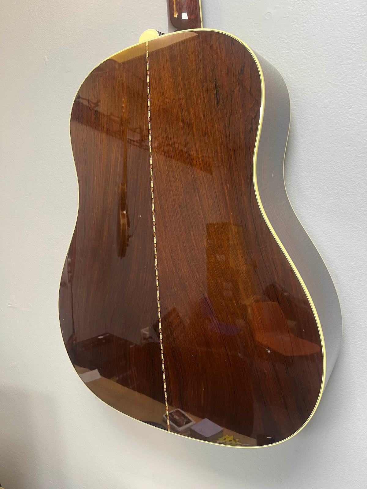 Back of a 2005 Collings CJ BaA acoustic guitar (Brazilian rosewood & Adirondack spruce) with a glossy dark wood finish, cream binding, and decorative center seam, shown against a plain light wall.