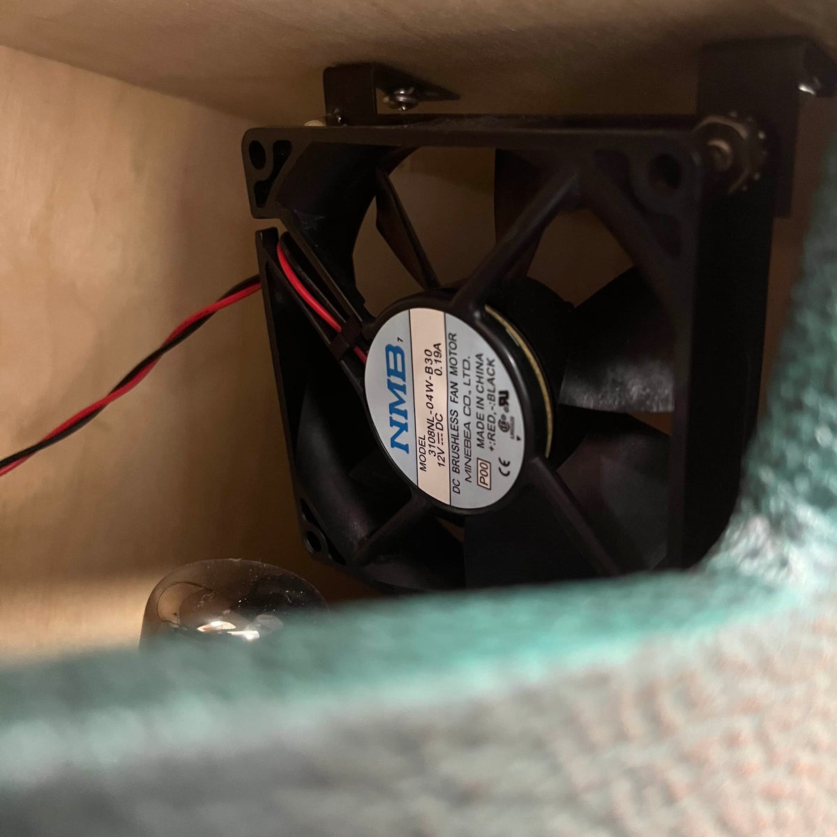 A close-up of a cooling fan with model info on the label, mounted inside a 2005 Divided by 13 RSA 31 Head with Matching 2x12 Cabinet and Flight Case by Divided by 13, with wires attached.