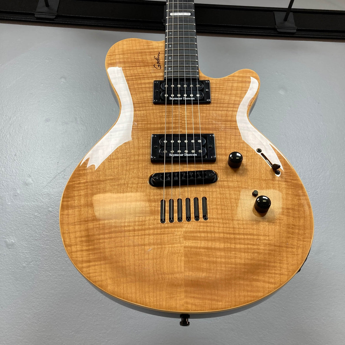 The 2009 Godin Summit CT w/Carved Flame Maple Cap electric guitar by Godin features a natural wood finish, two Seymour Duncan humbuckers, two control knobs, a switch, and a distinctive bridge, photographed against a gray wall.