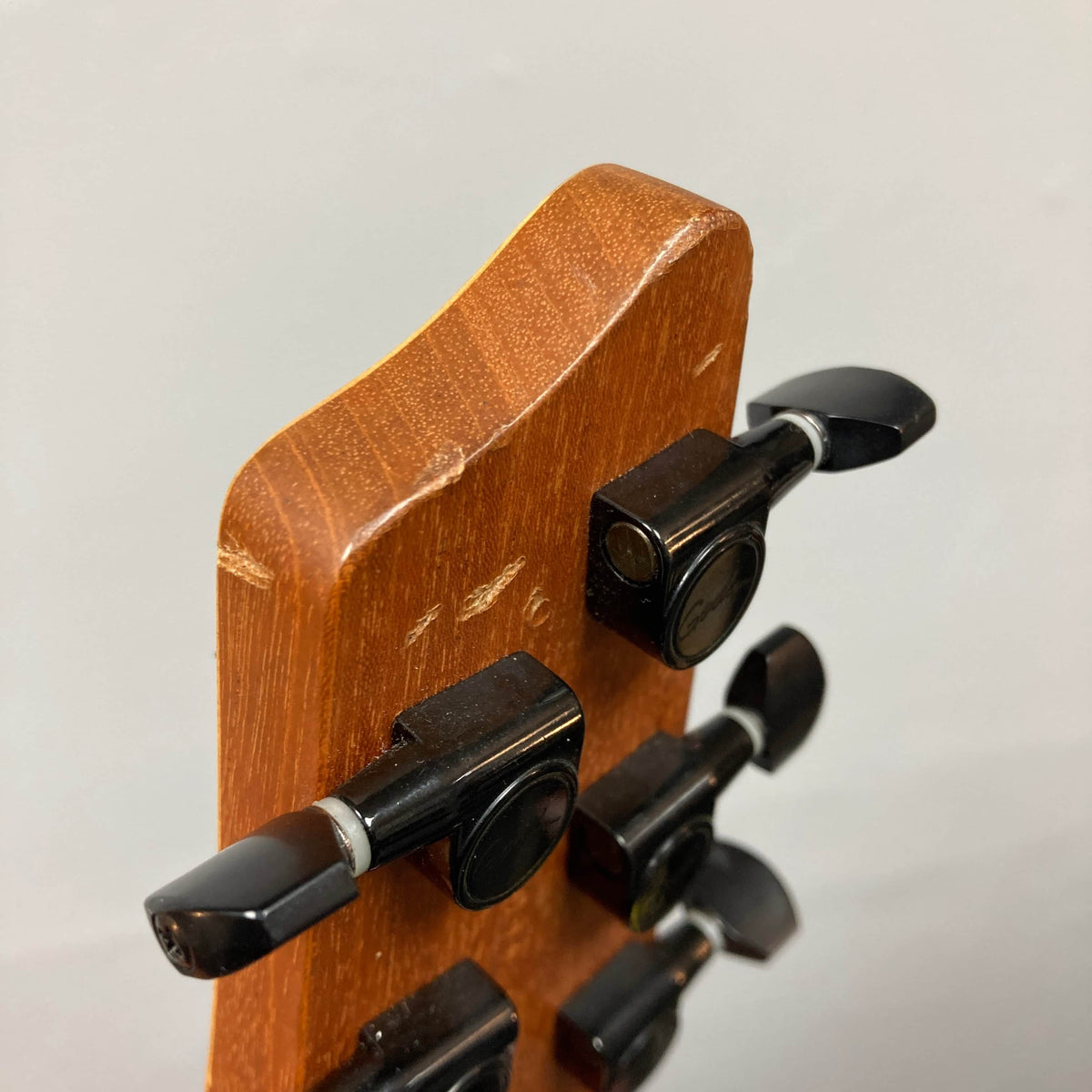 Close-up of the back of a 2009 Godin Summit CT w/Carved Flame Maple Cap headstock, featuring four black tuning pegs and visible scratches on the wood surface.