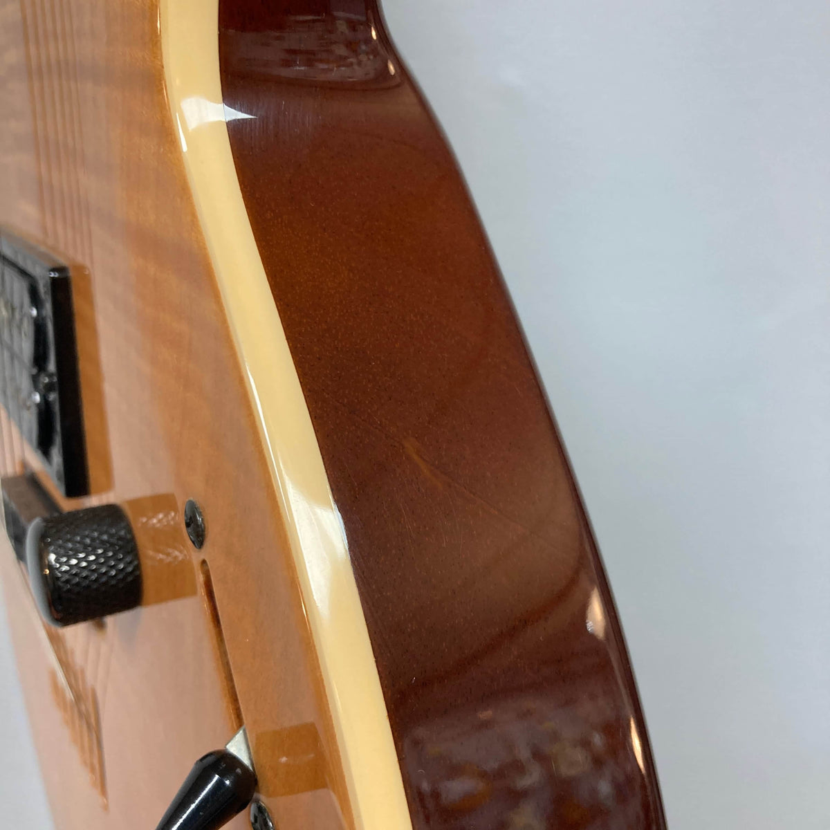 Close-up of the side and edge of a 2009 Godin Summit CT w/Carved Flame Maple Cap electric guitar, showing the flame maple top, control knob, and some visible surface scratches.