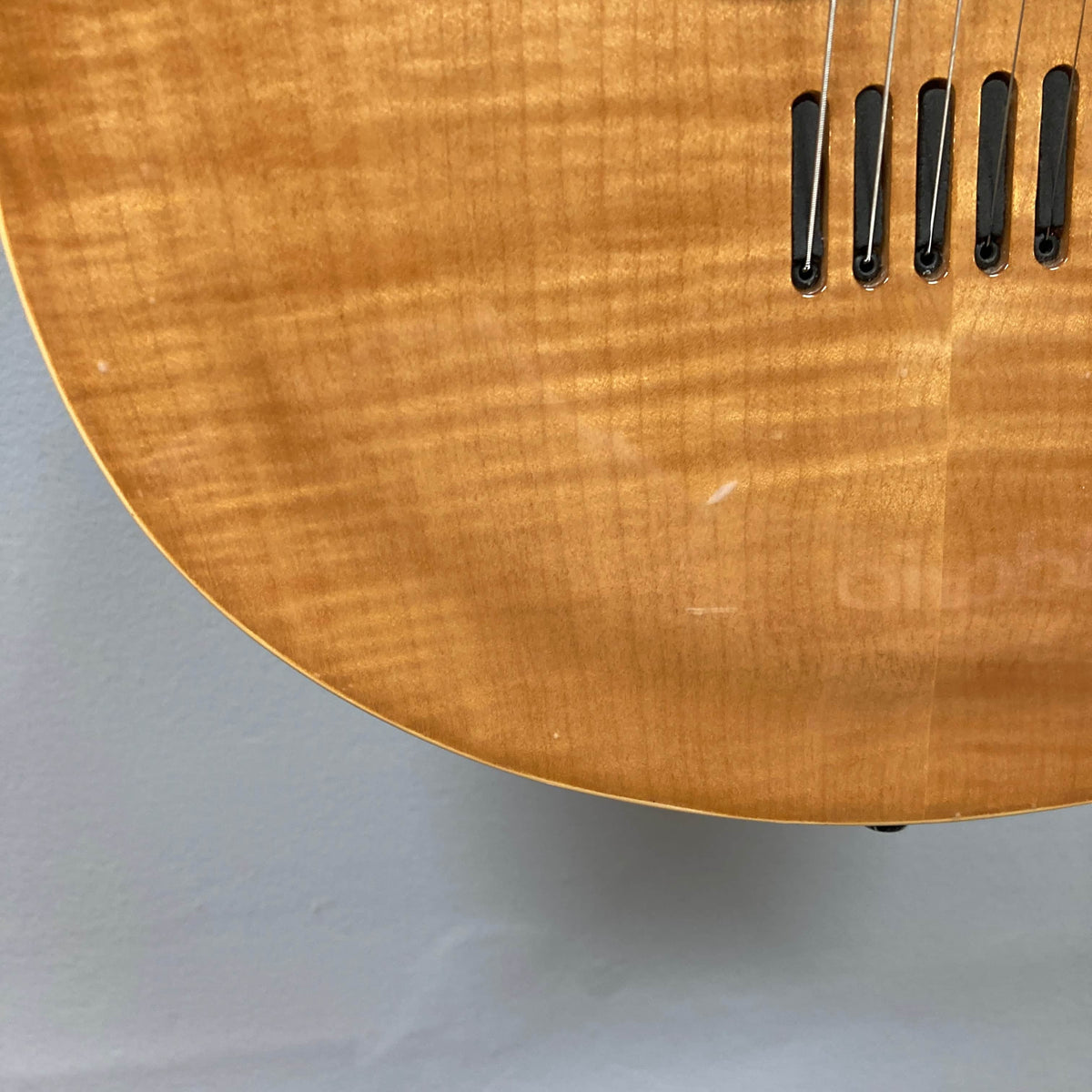 Close-up of the lower body of a 2009 Godin Summit CT electric guitar, highlighting its carved flame maple cap, bridge, strings, and unique wood grain pattern.